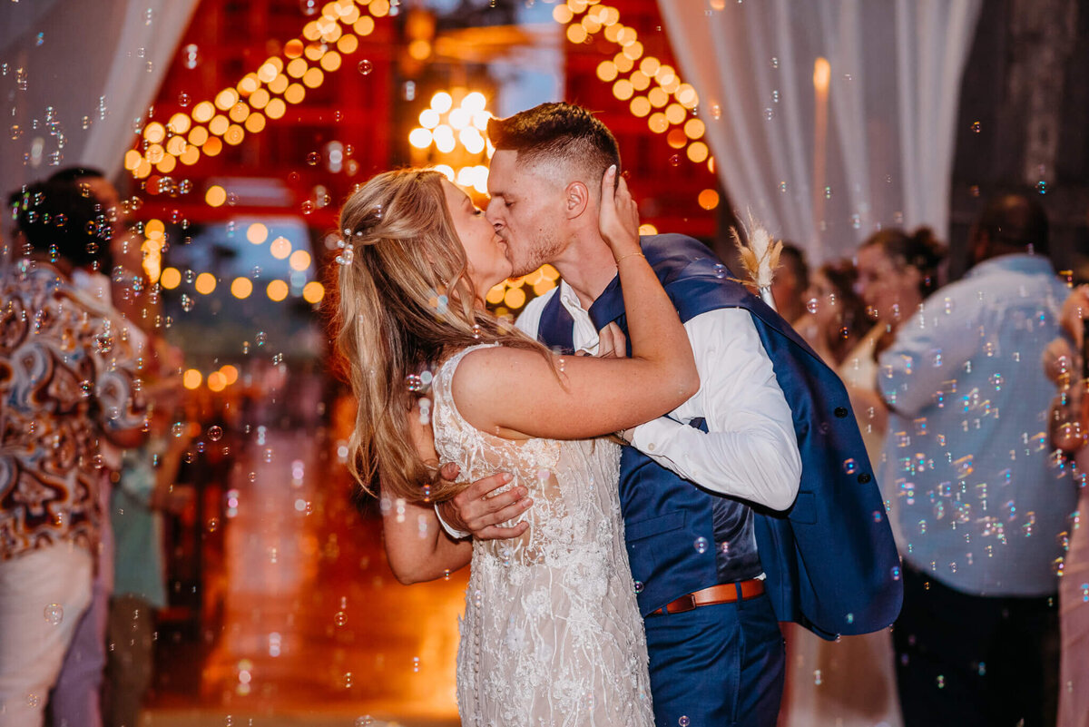 Photo of a bride and groom kissing in a tunnel of bubbles with lights in the background