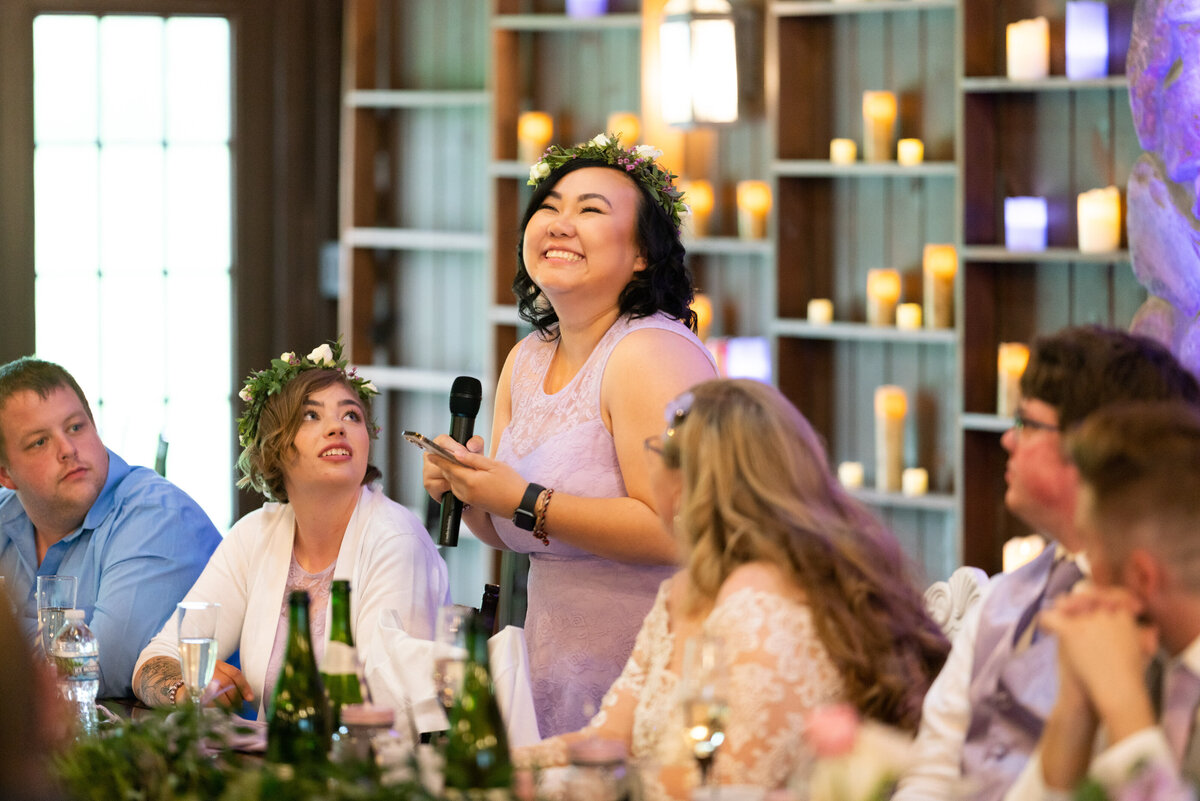 Bridesmaid laughs during wedding speech at head table.