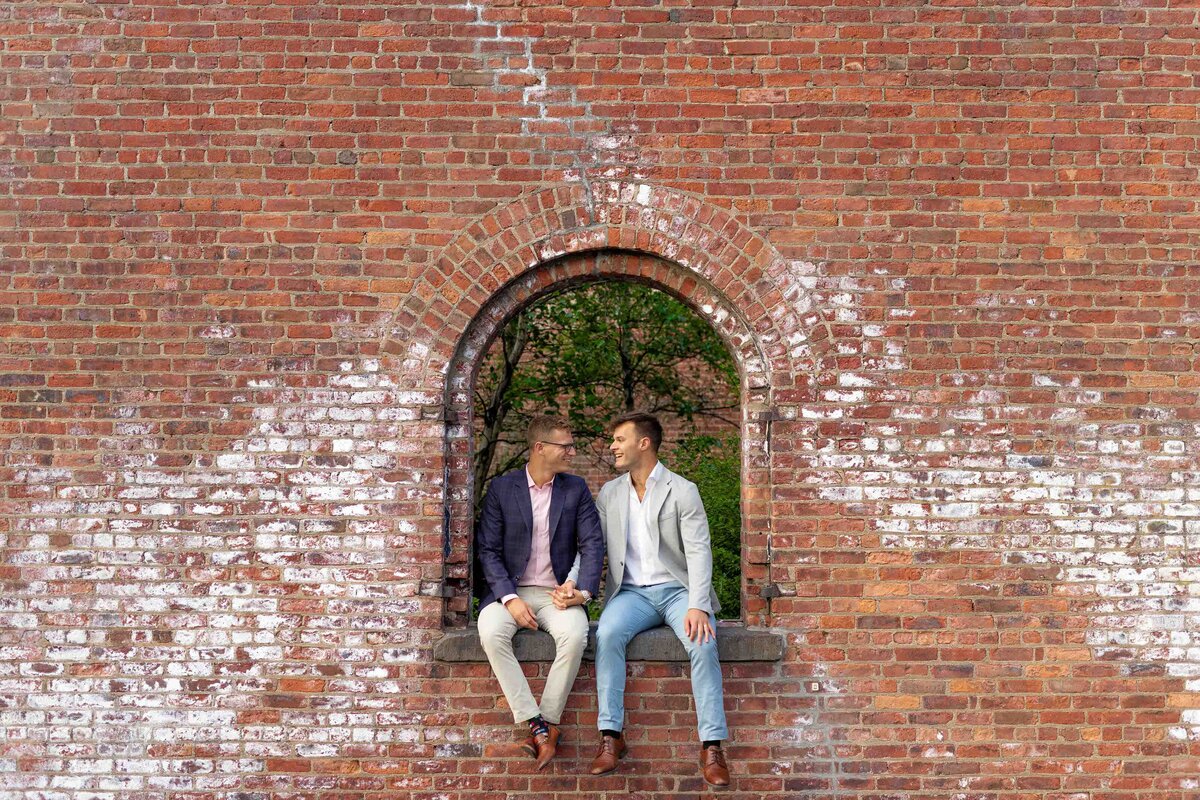 Two people sitting in a small arch in a brick wall.