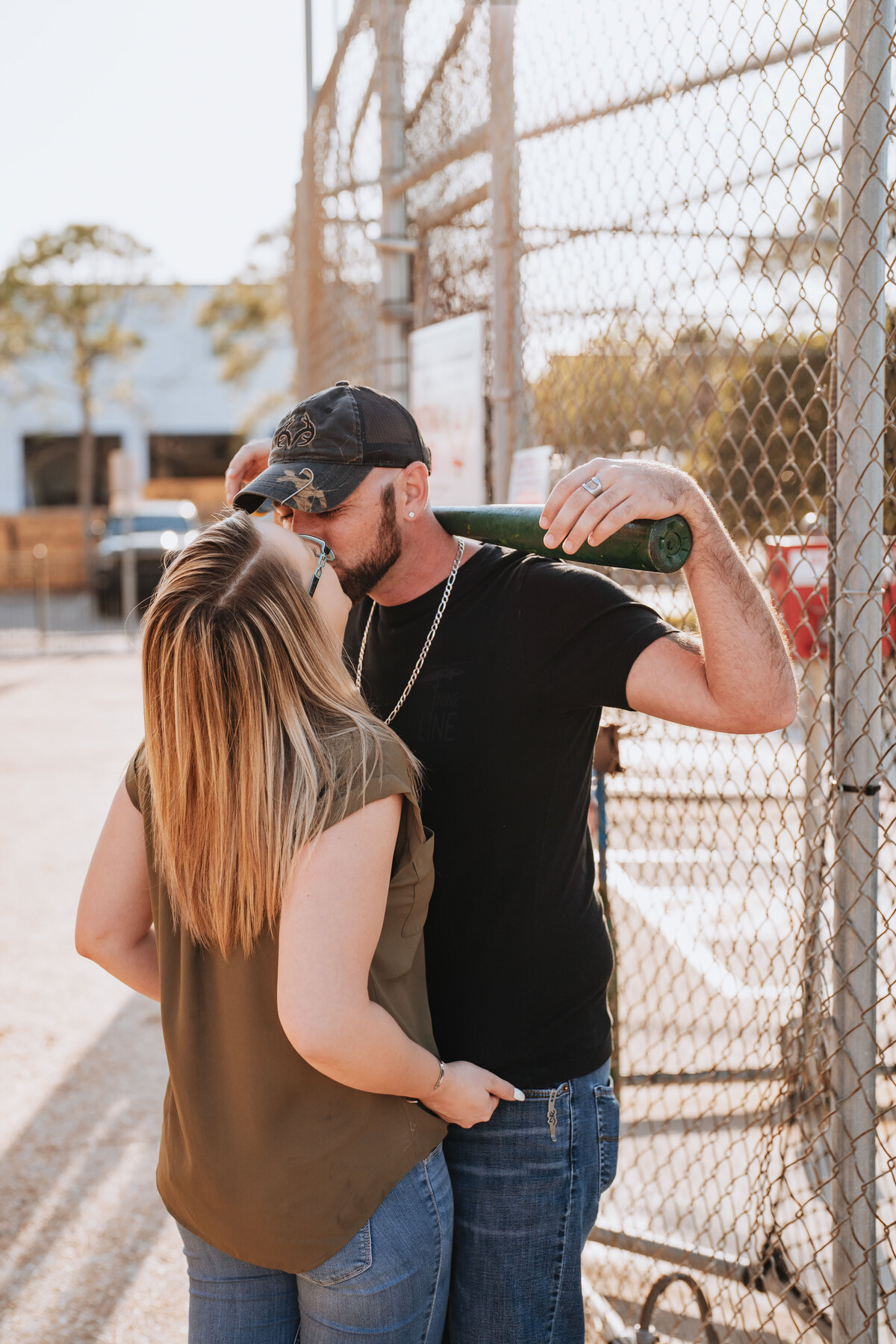 couple kissing on batting cages during engagement session at celebration station in clearwater florida
