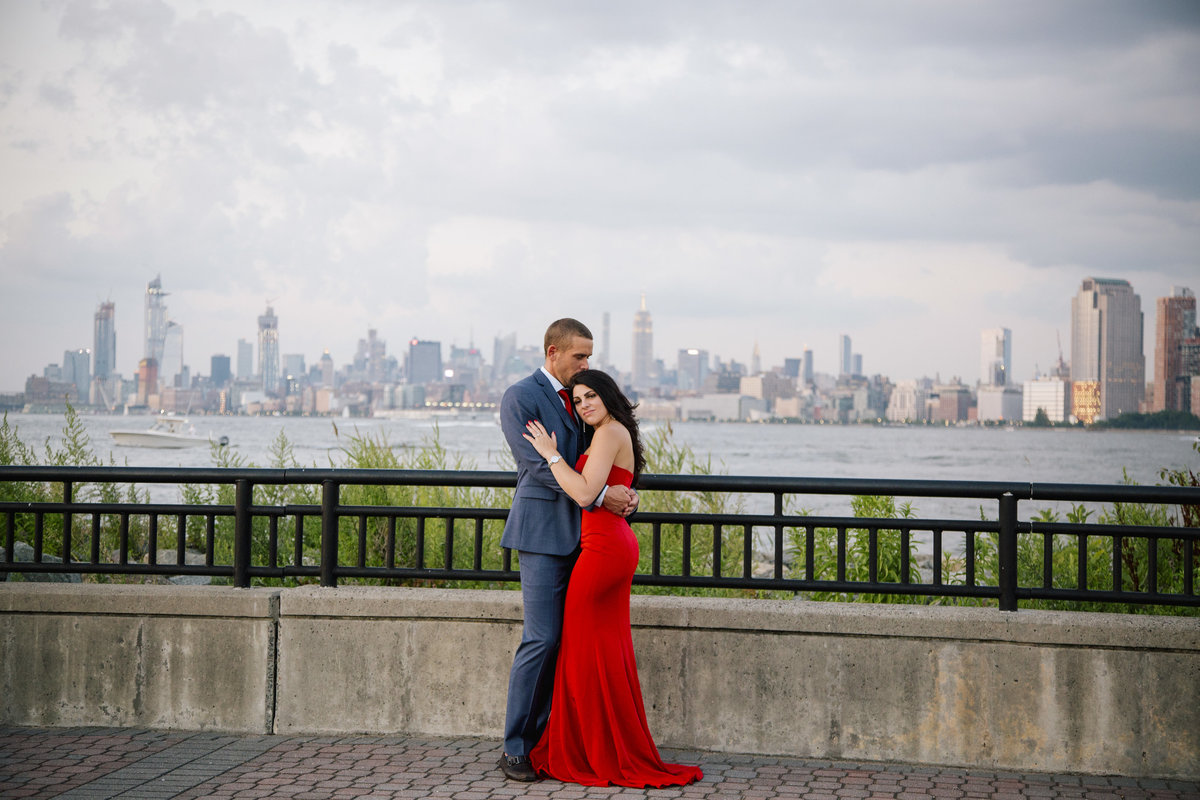 engaged couple hug by nyc skyline  at liberty state park