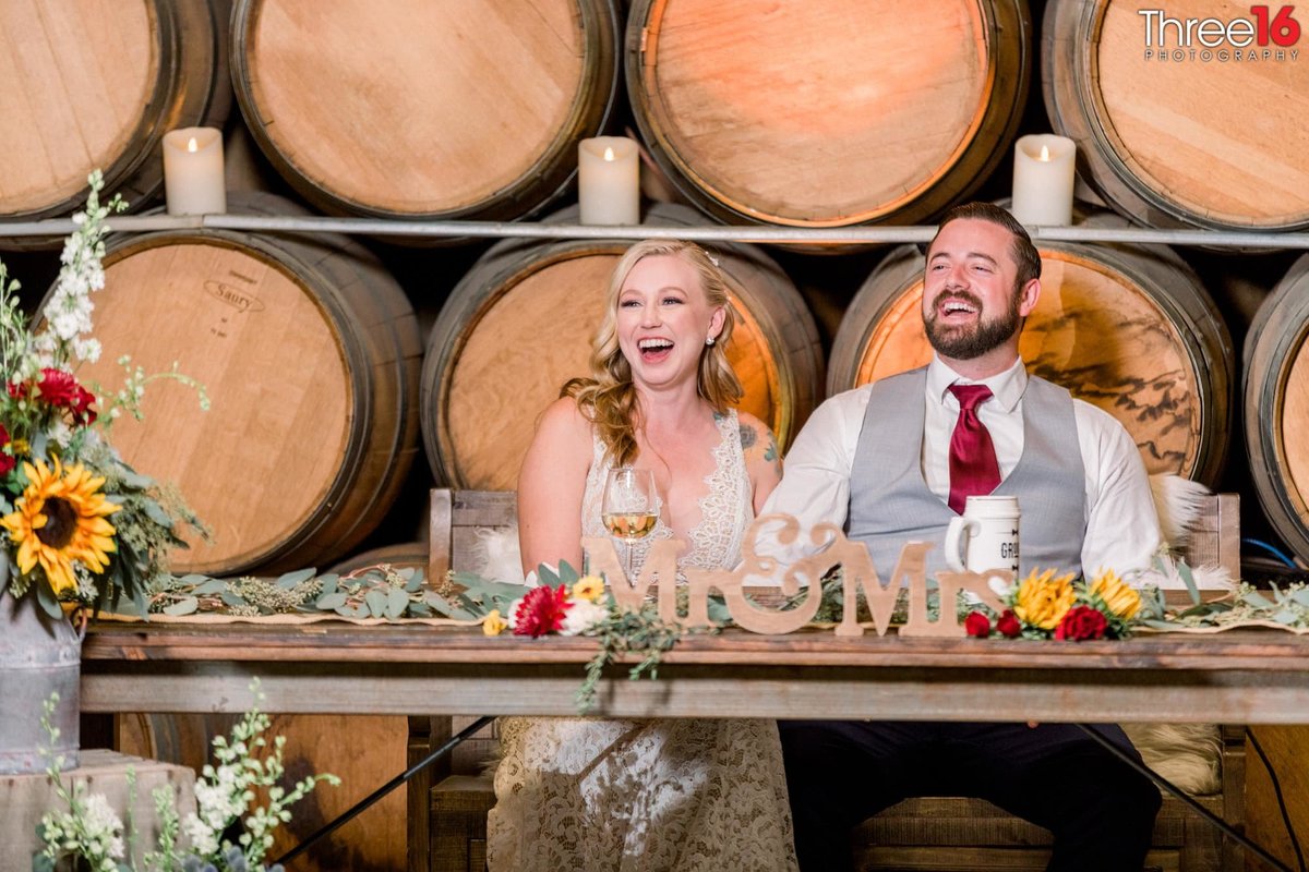 Bride and Groom sit at the sweetheart table during the reception and laugh at the best man's toast