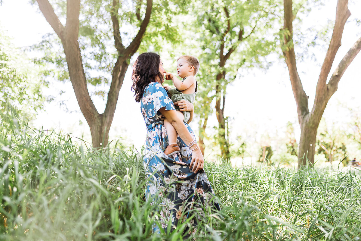 Maternity Photographer, a mother walks through tall grass holding her baby