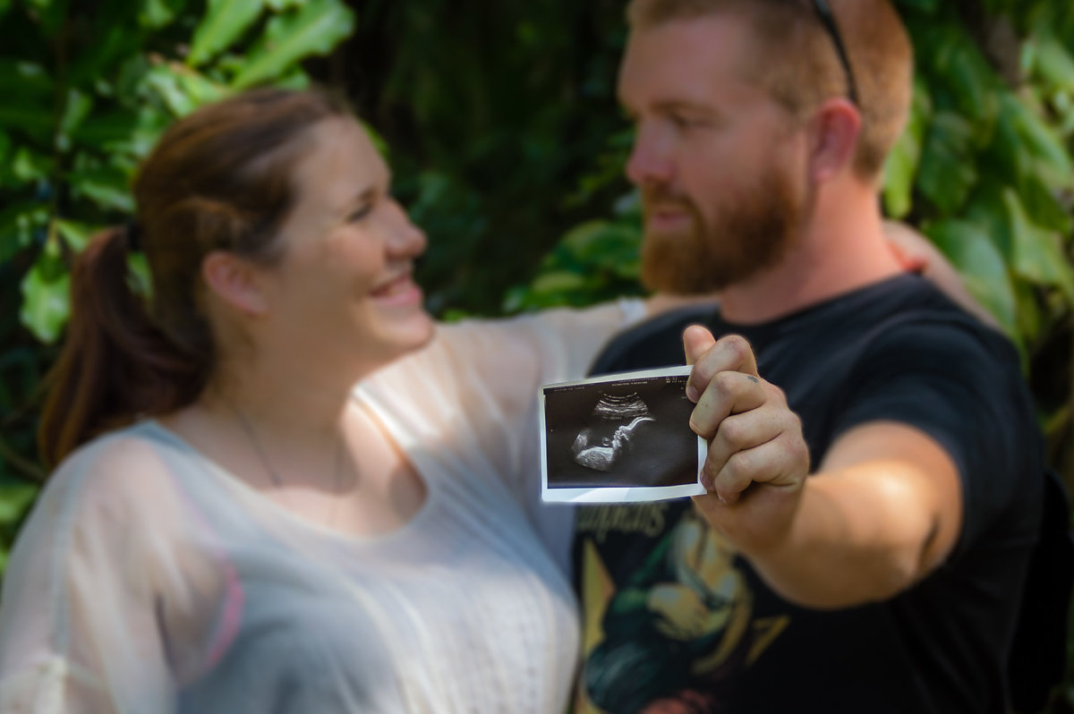 A soon-t-be dad holds the ultrasound photo while looking at soon-to-be mom