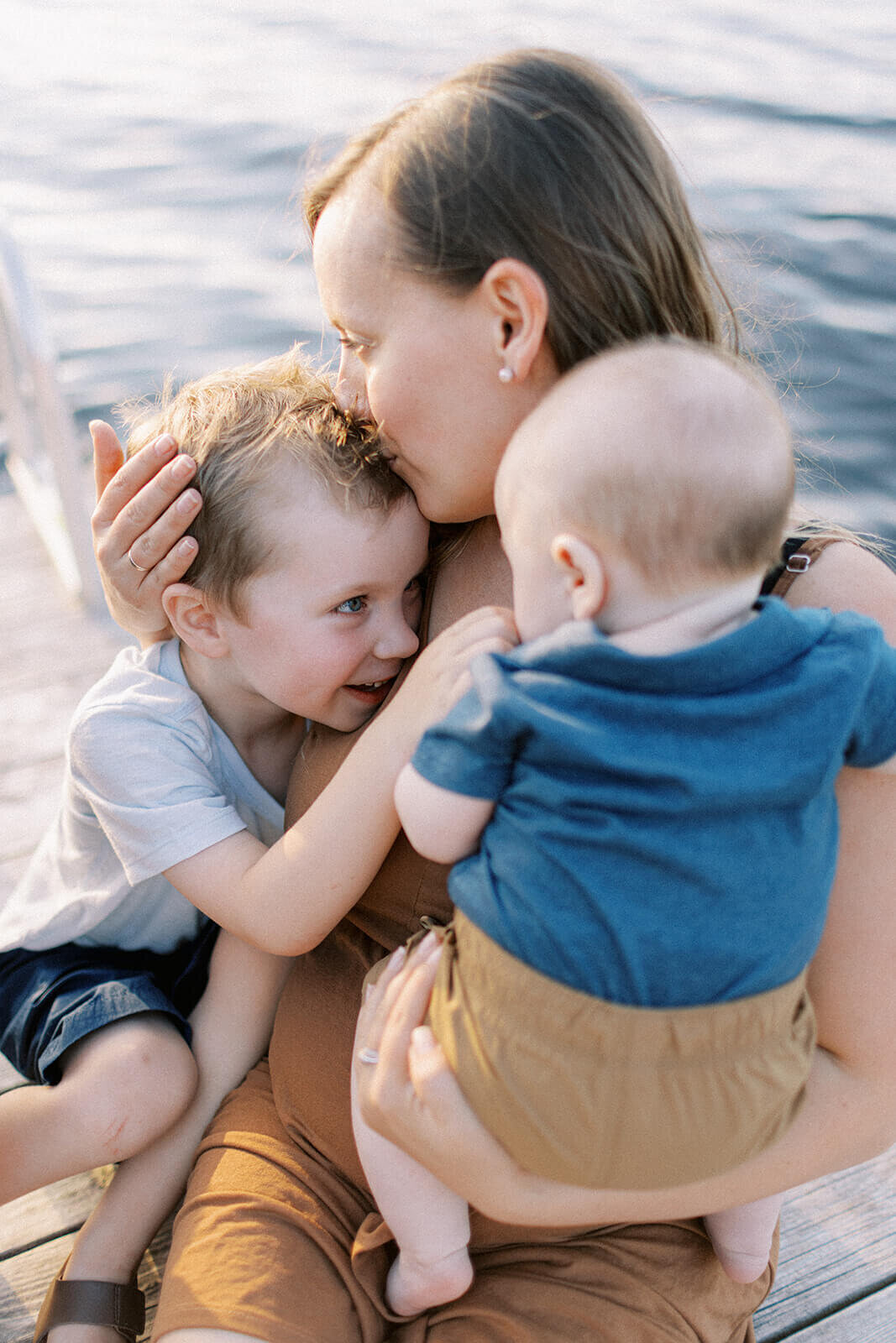 mother-holds-two-kids-and-kisses-childs-forehead
