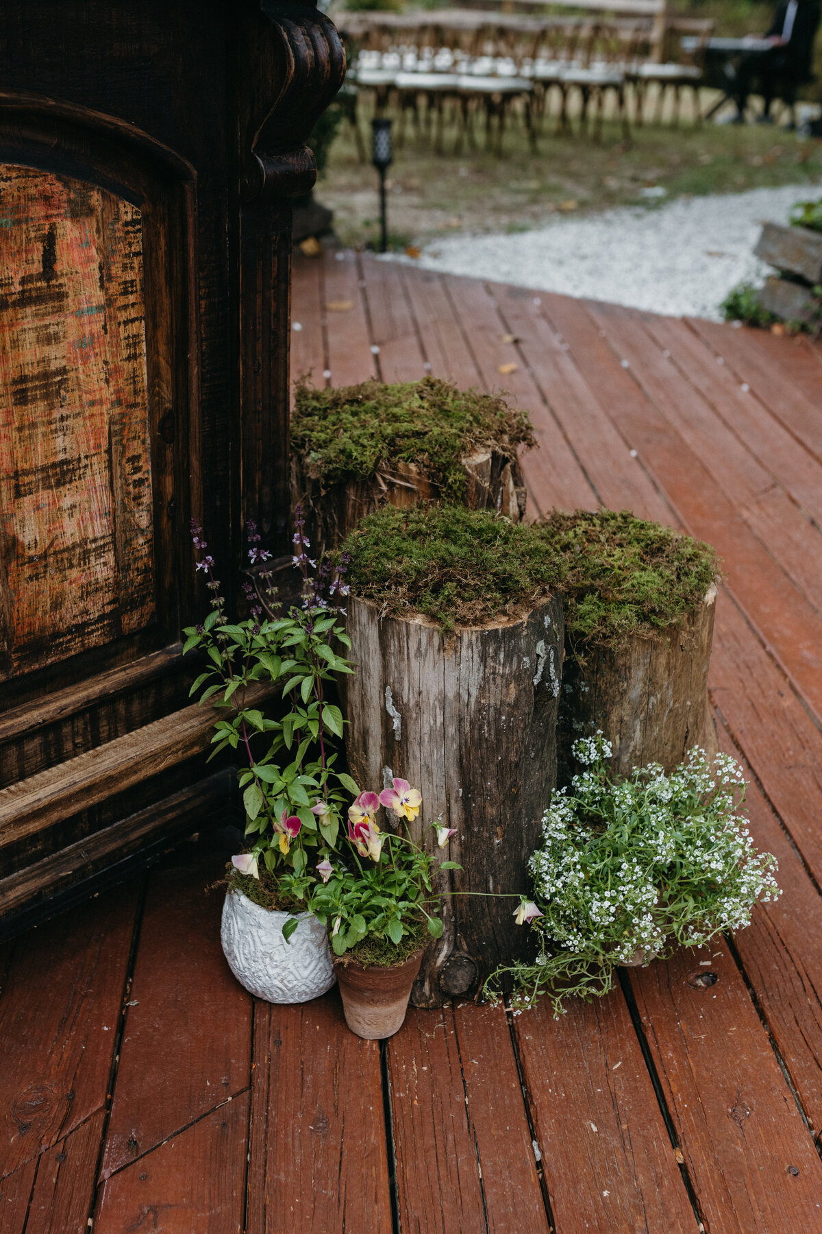 Woodland-inspired wedding décor with moss-covered tree stumps and potted seasonal flowers arranged near the reception deck at The Nest in Northwest Arkansas.