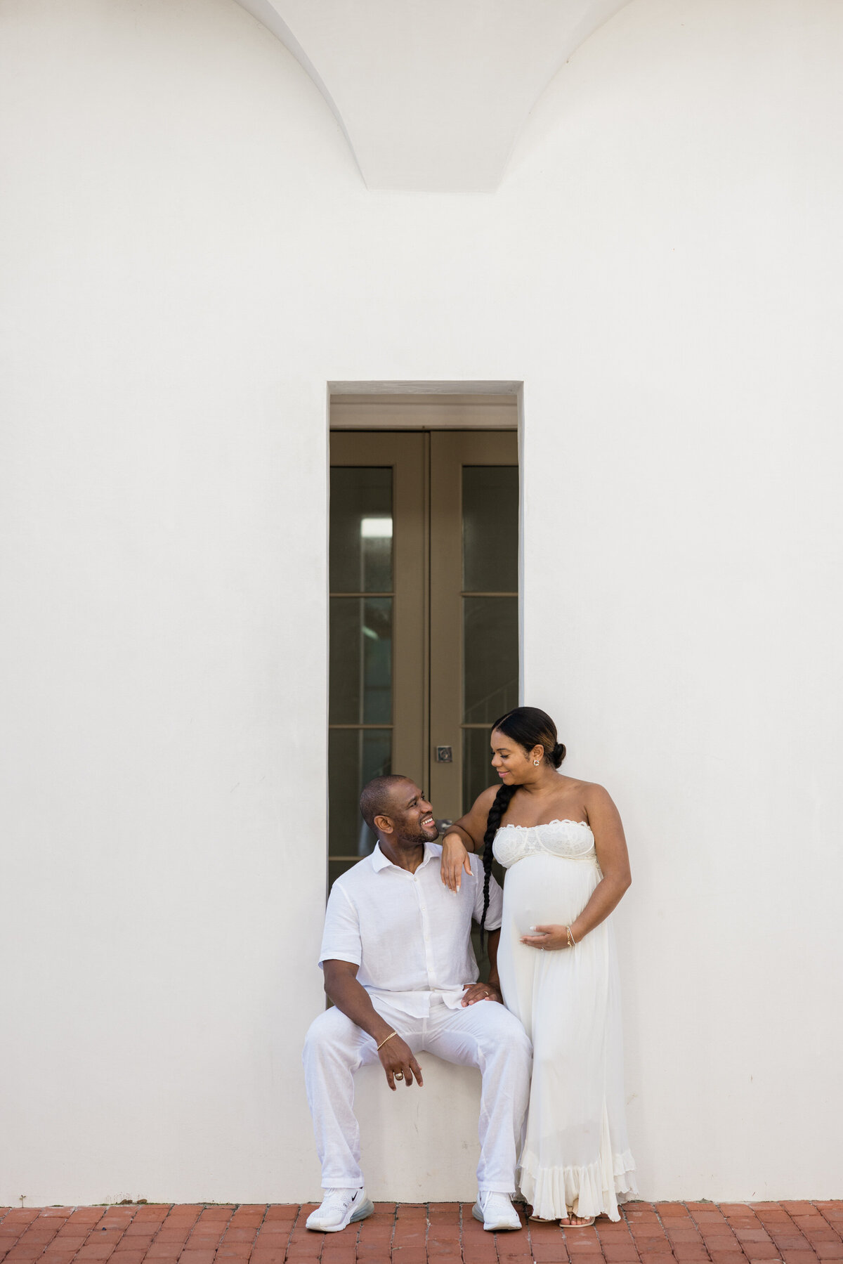 A person sitting in a windowsill with their pregnant partner standing next to them