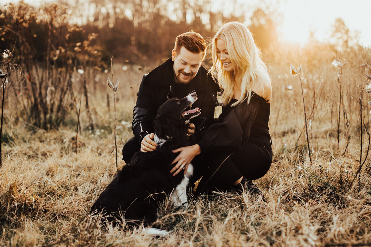 couple petting their dog in grass at sunset