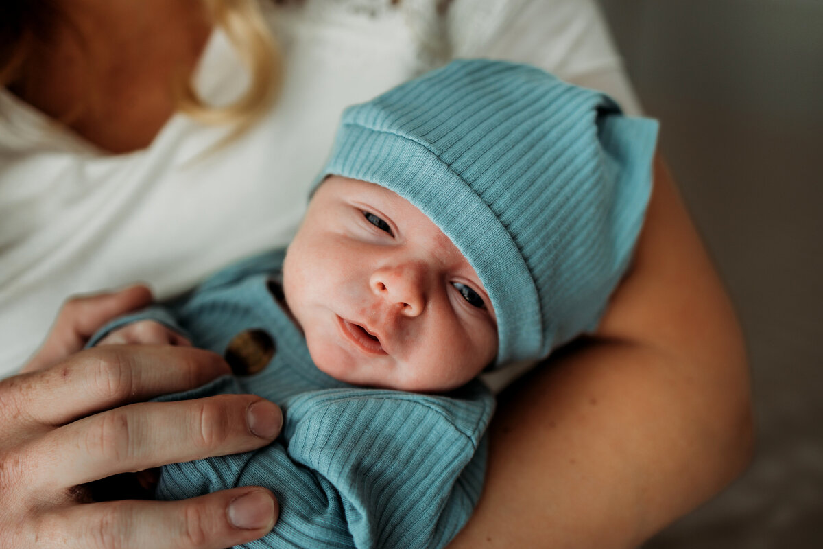 mom holding a newborn baby boy in blue sleeper sack and stocking cap