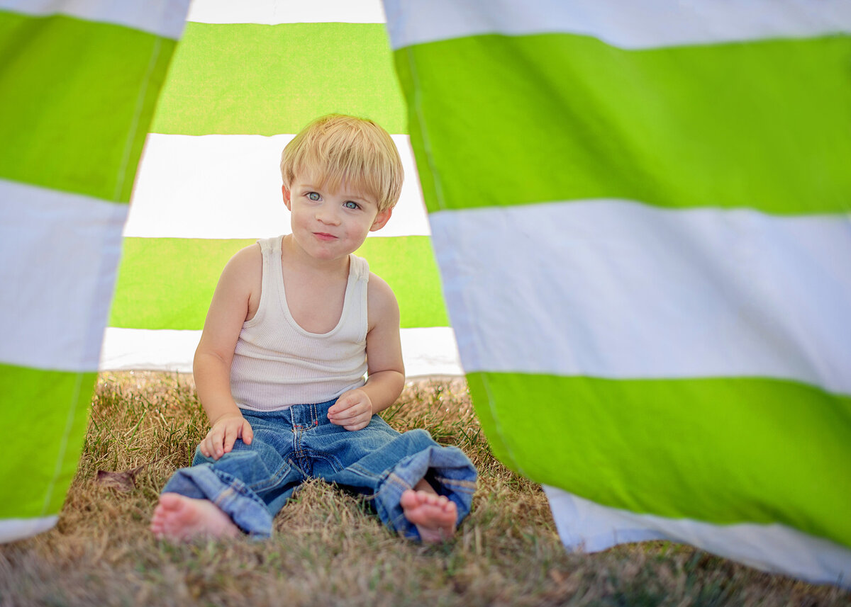 little blond boy in white tank top and jeans in green and white striped tent