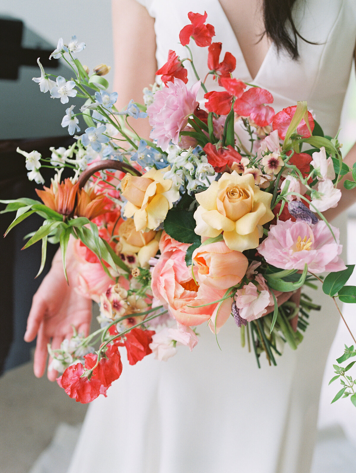 A bride holds a large bouquet of very colorful flowers in a Dutch Masters style by Anthousai Florals, in Tulsa.