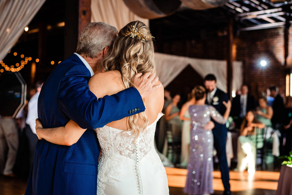 Father of the bride hugging his daughter while her husband and his mom share a dance together