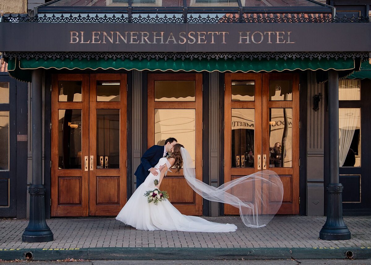 bride and groom kiss with veil flows in wind in front of Blennerhassett hotel