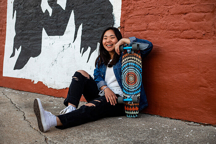 girl-sits-with-skateboard-against-brick-wall