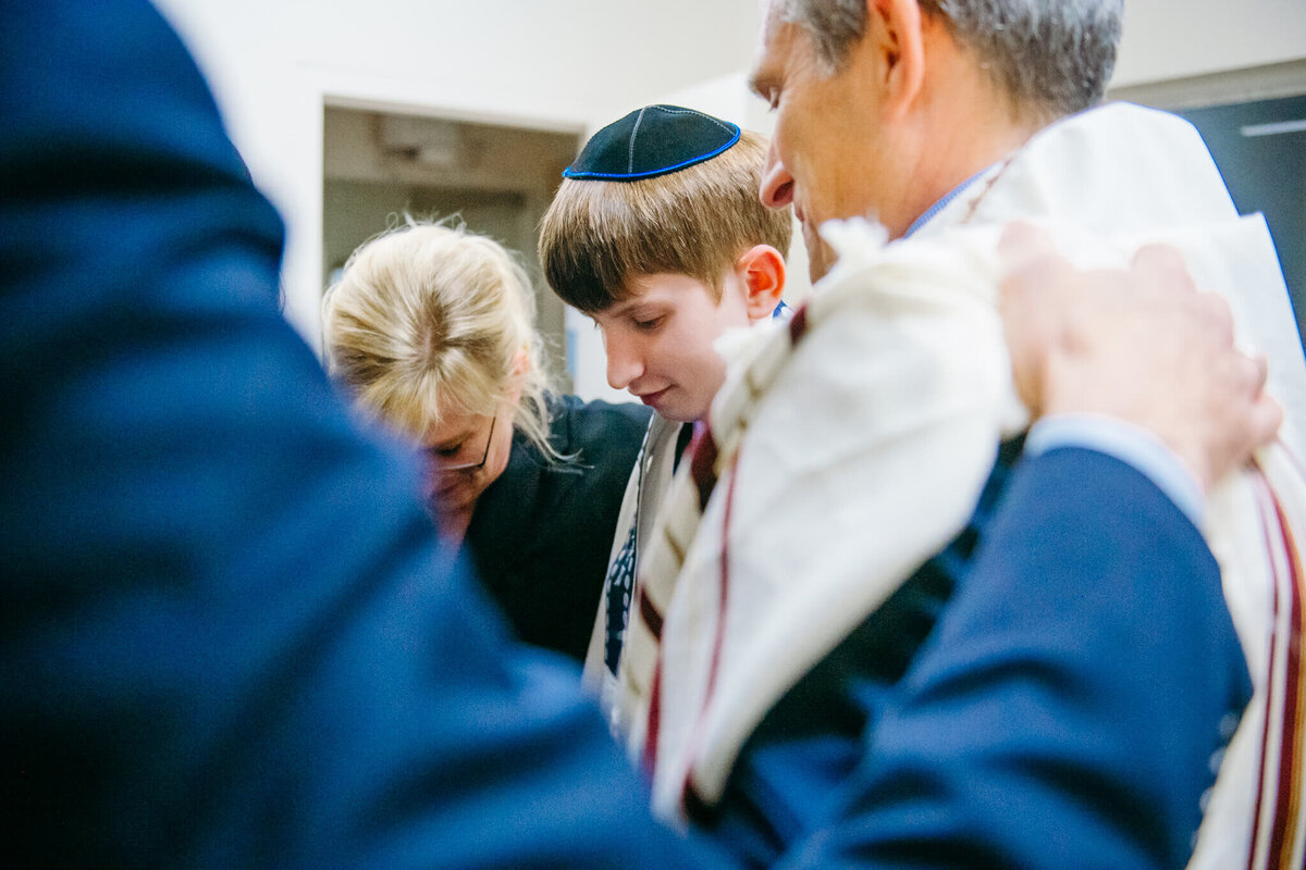 A boy stands with his parents and rabbi praying before his bar mitzvah
