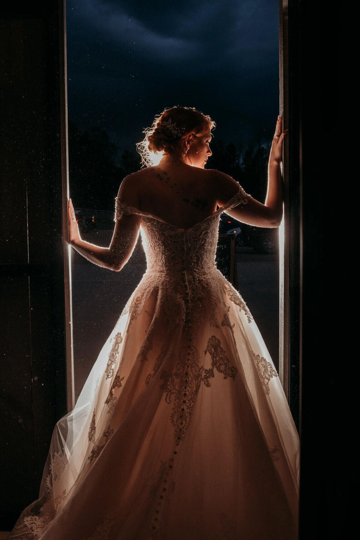 Photo of a bride's silhouette from behind as she holds the barn doors