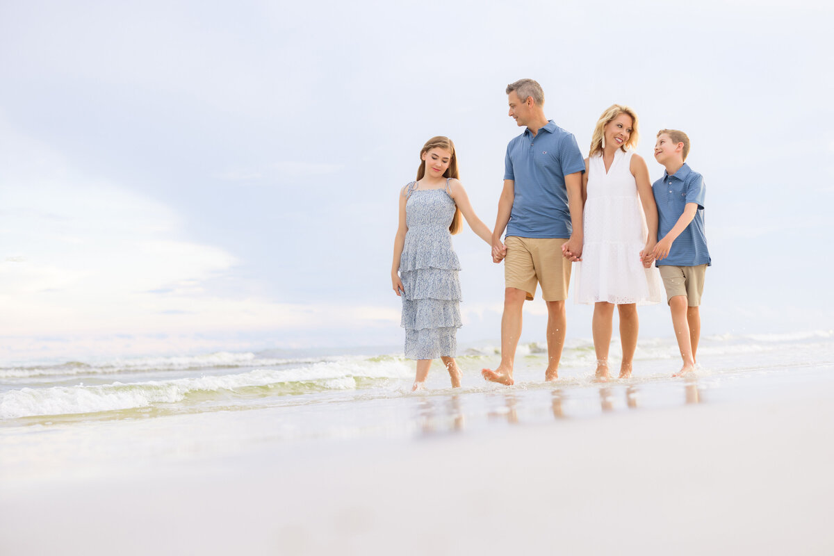 Parents holding hands with their kids and walking along the water