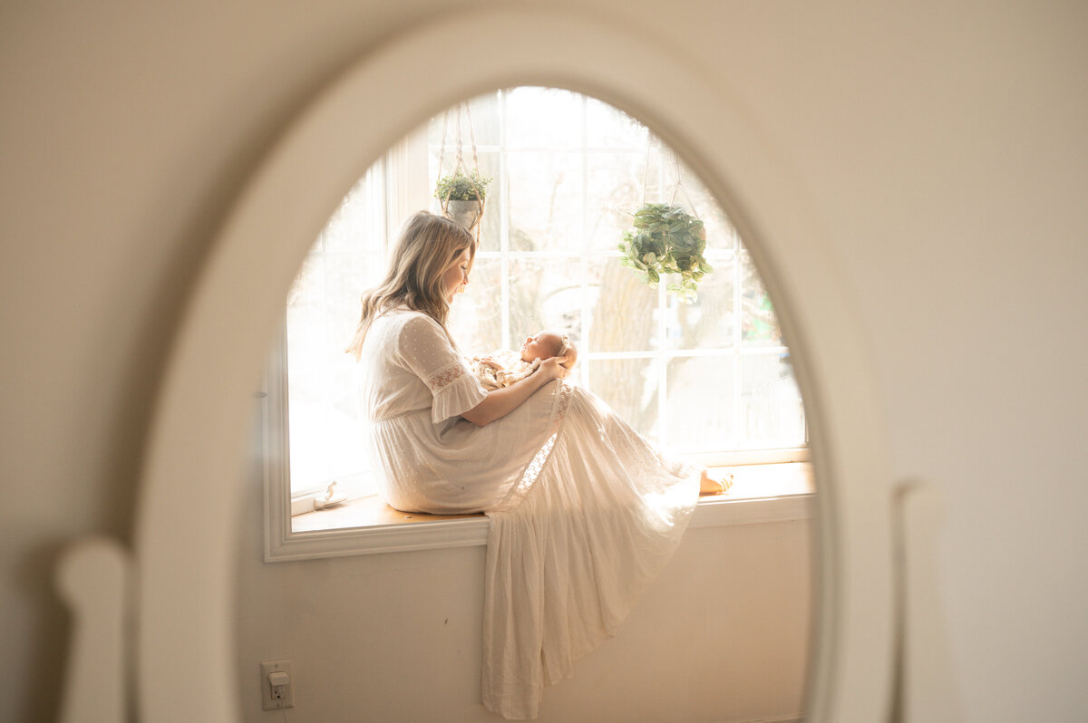 Mother sitting on a window sill holding her newborn baby