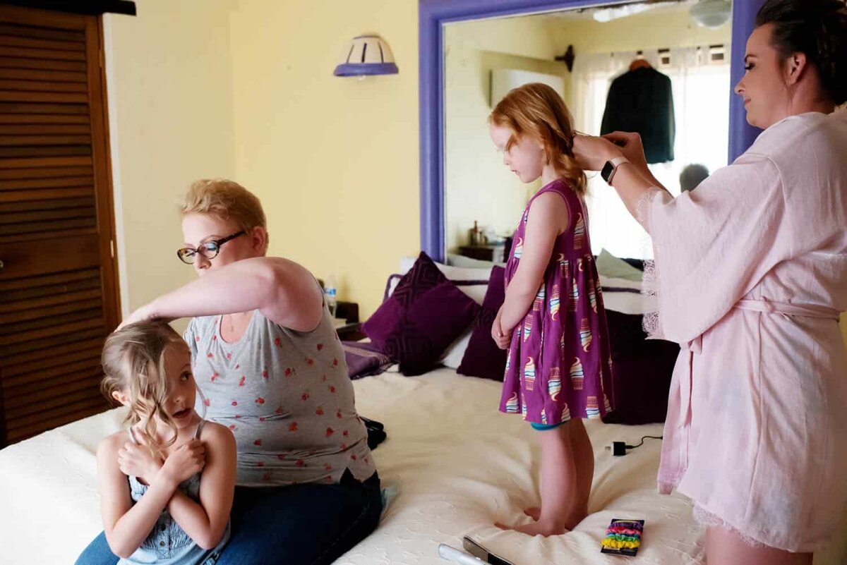 two women curl the hair of 2 little girls before a wedding