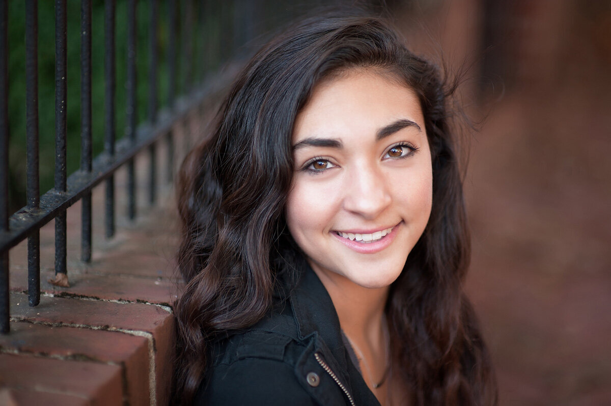 Senior session of young woman sitting near a fence