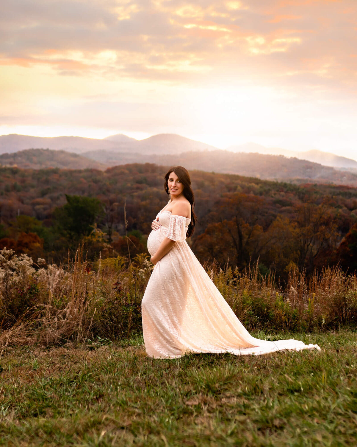A young expecting woman stands on a mountain top as her white gown blows in the wind