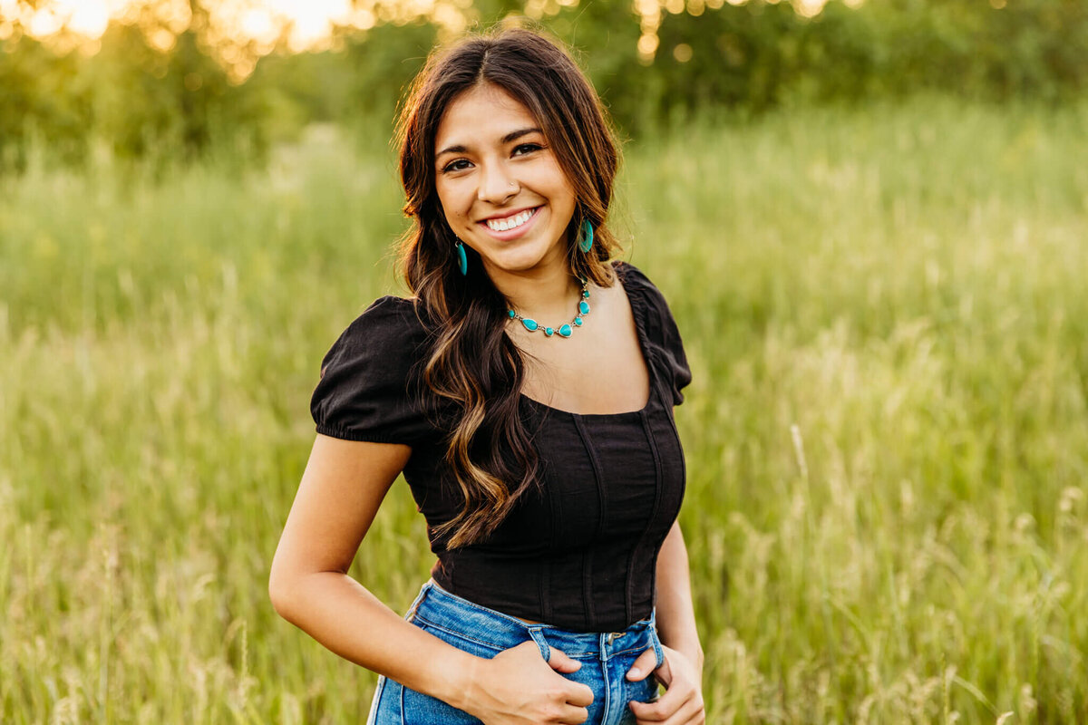 stunning senior in a black shirt, jeans and turquoise jewelry smiling for her senior photography session  with Ashley Kalbus