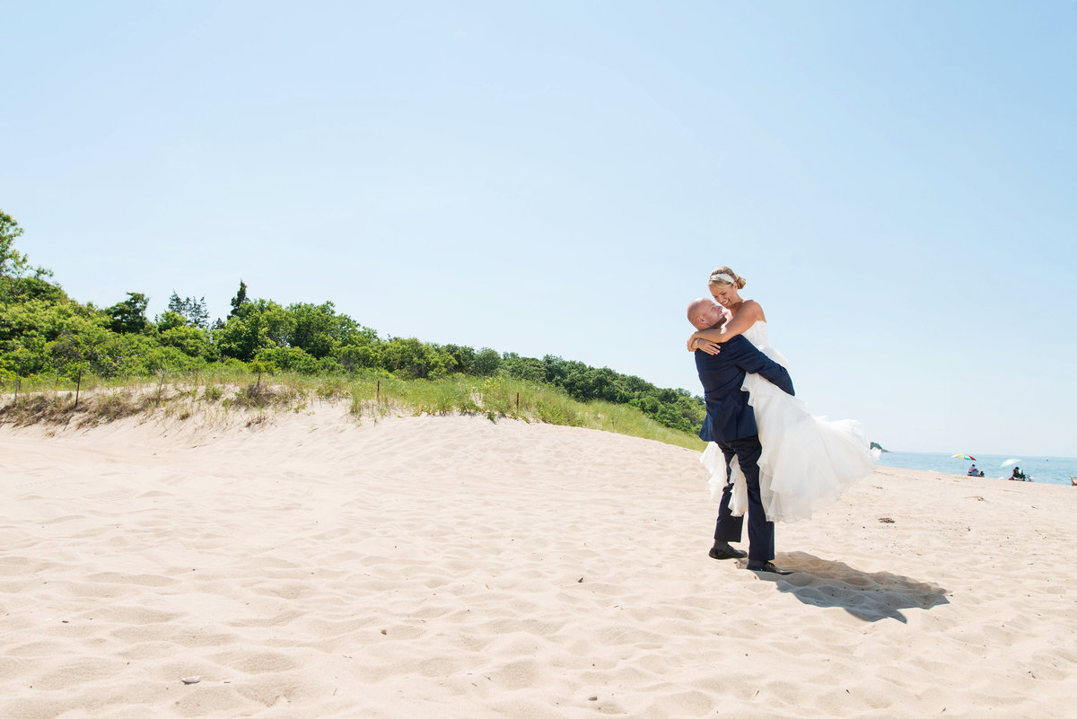 photo of groom holding his bride in the air on the beach from wedding reception at Pavilion at Sunken Meadow