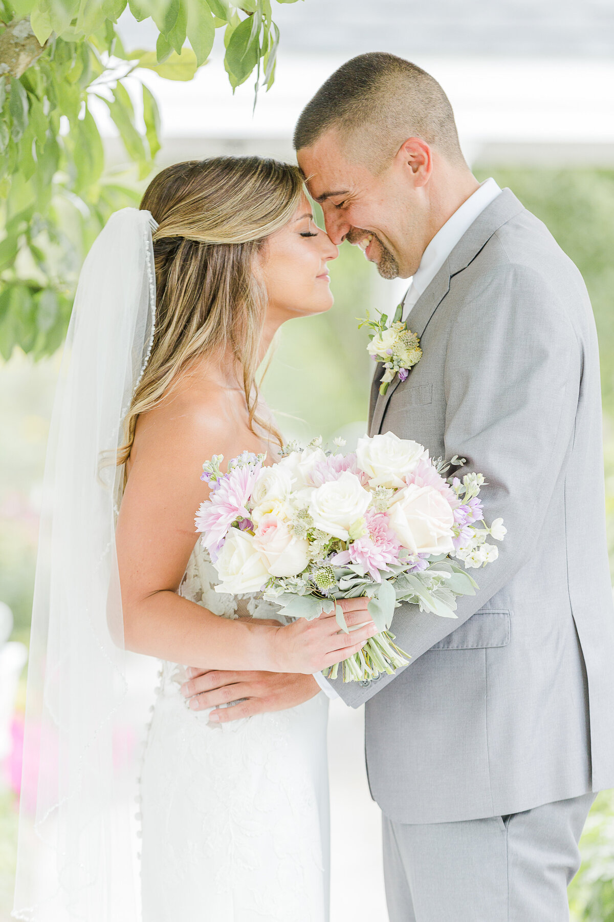Bride and groom touch noses with their eyes closed for an intimate wedding portrait. The bride is holding her flowers in the foreground. Captured by best Massachusetts wedding photographer Lia Rose Weddings.