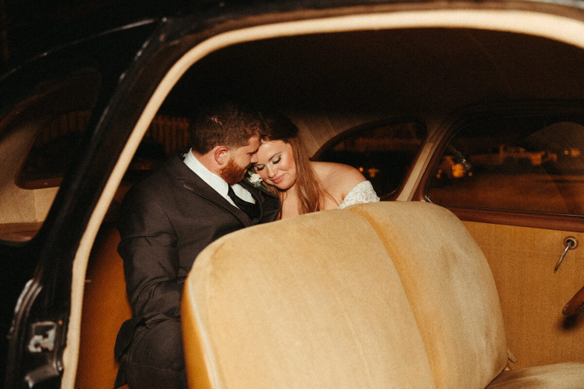 Bride and groom in the backseat of an old vintage getaway car