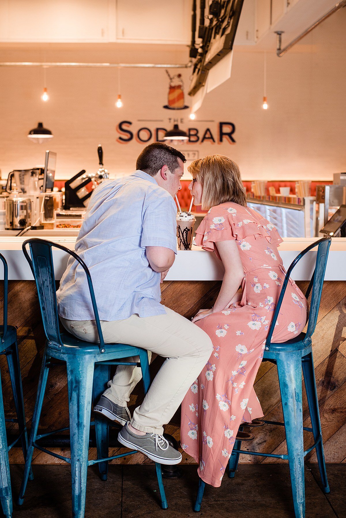 Couple sharing a milkshake outside of the Soda Bar in Murfreesboro TN, seated on two stools and sipping from straws