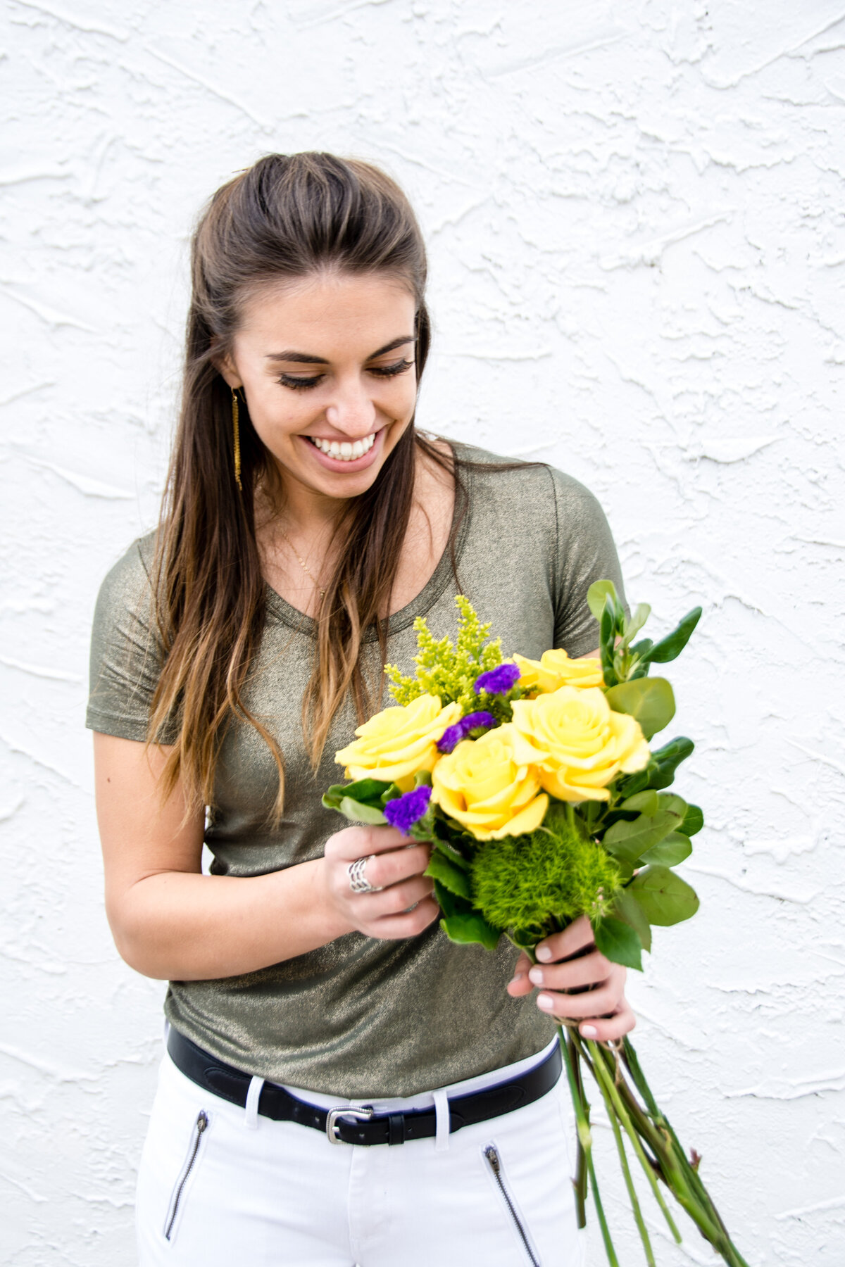 Smiling woman looks down at a bouquet of yellow and purple flowers
