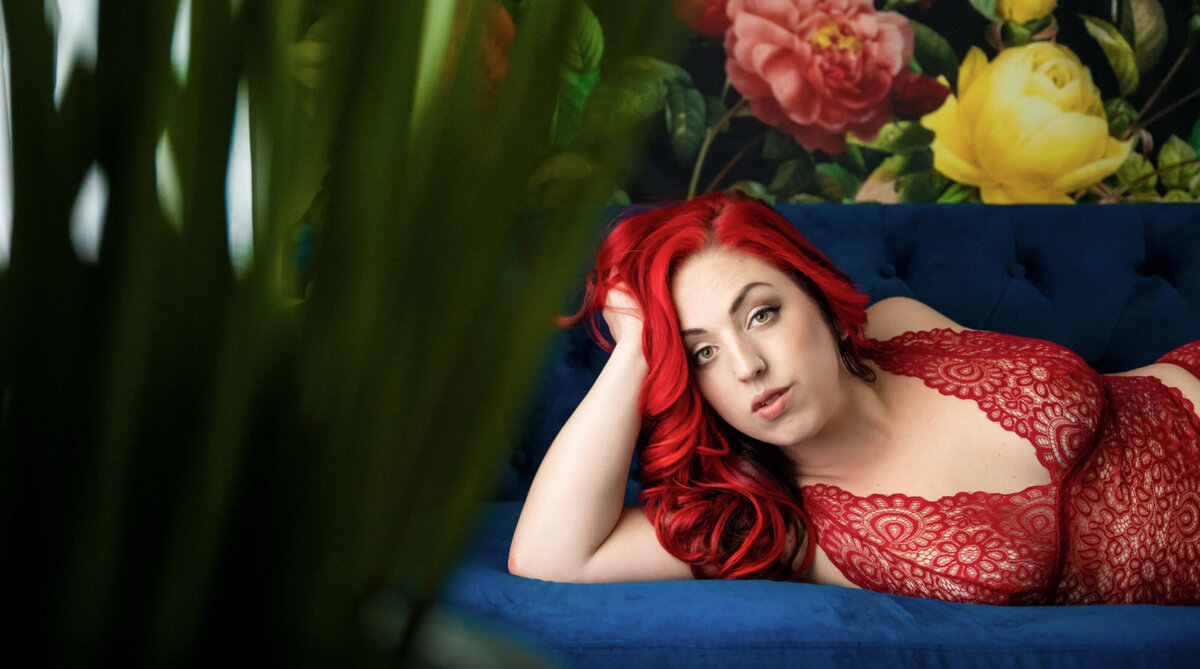 Woman posing for a boudoir photo with bright red hair that matches her red lingerie