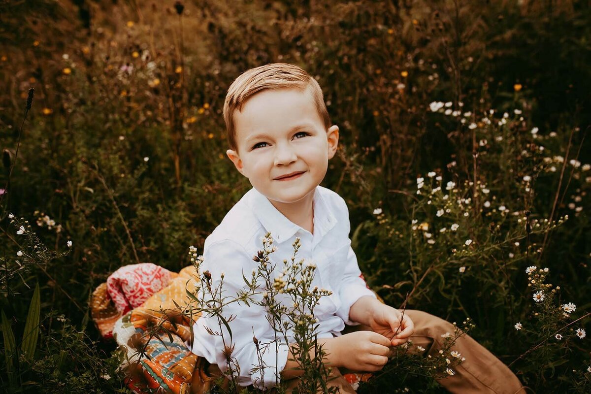 a little boy sitting in a field of flowers at sunset