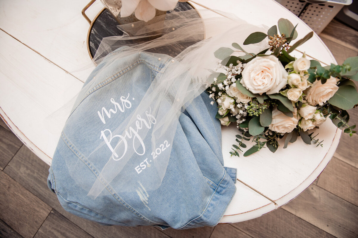 Brides bouquet, veil and jean jacket on a  white tabletop