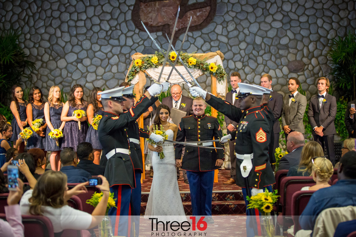 In his military uniform Groom escorts his Bride down the aisle as military hold swords over their heads as they leave the Calvary Chapel wedding venue in Murrieta