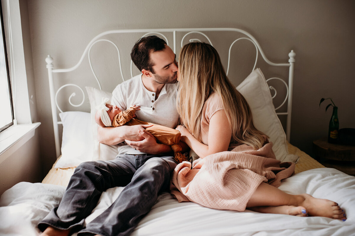 Newborn Photographer, Mom and dad snuggling with their baby in the bed.