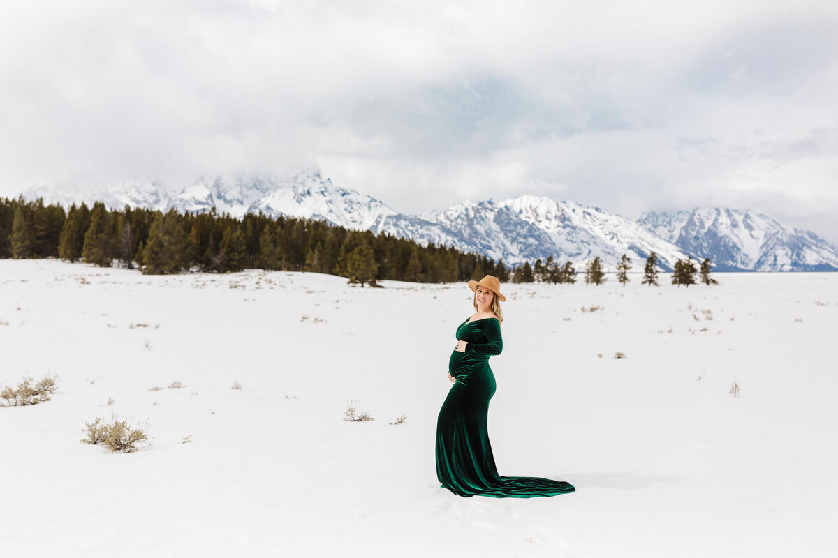Gorgeous pregnant mother in green gown standing in snow in Jackson Hole, Wyoming., Montana