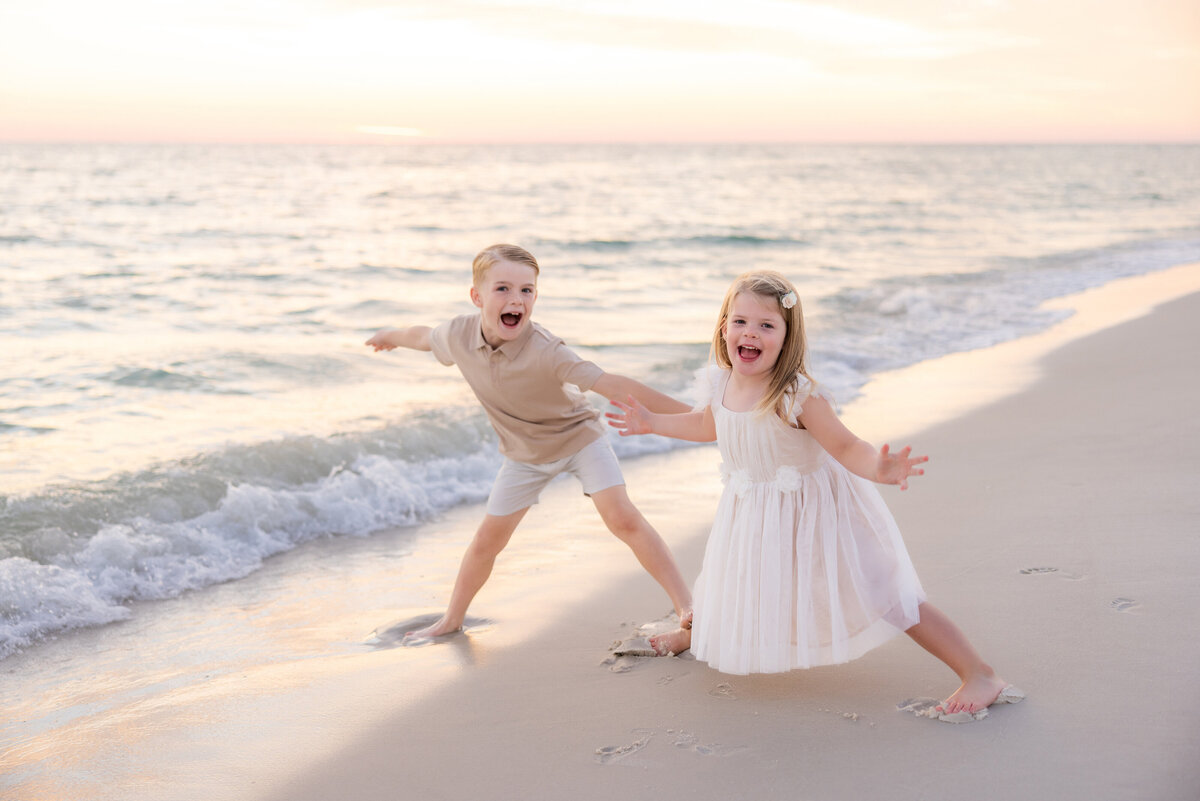 Two small kids smiling with their arms out at the beach