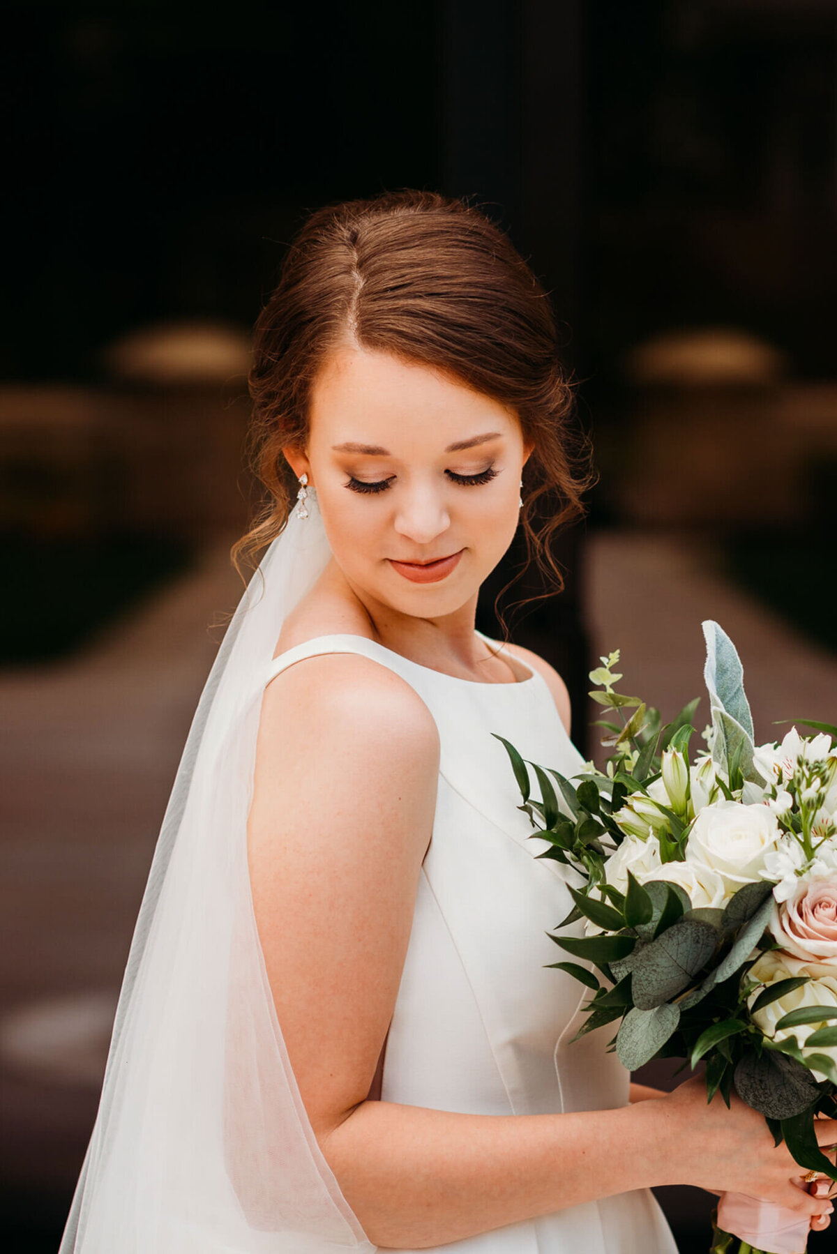 Photo of a bride holding her wedding bouquet and looking down at the ground