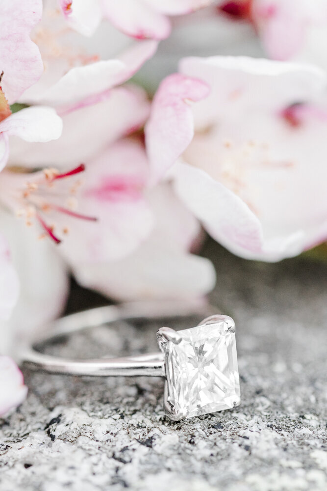 an engagement ring resting on a rock beside a flower