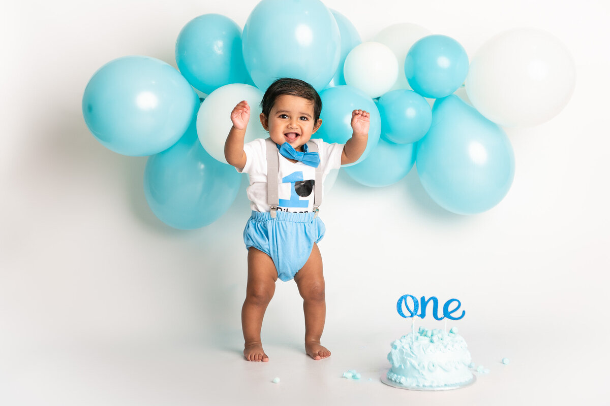 Baby with a blue cake and blue balloon garland