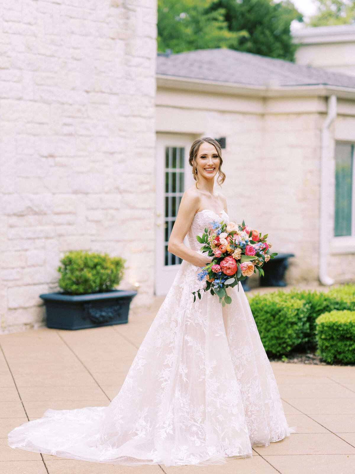 Elegant spring bride wearing Monique Lhuillier poses at Ashton Gardens wedding venue with rainbow bouquet