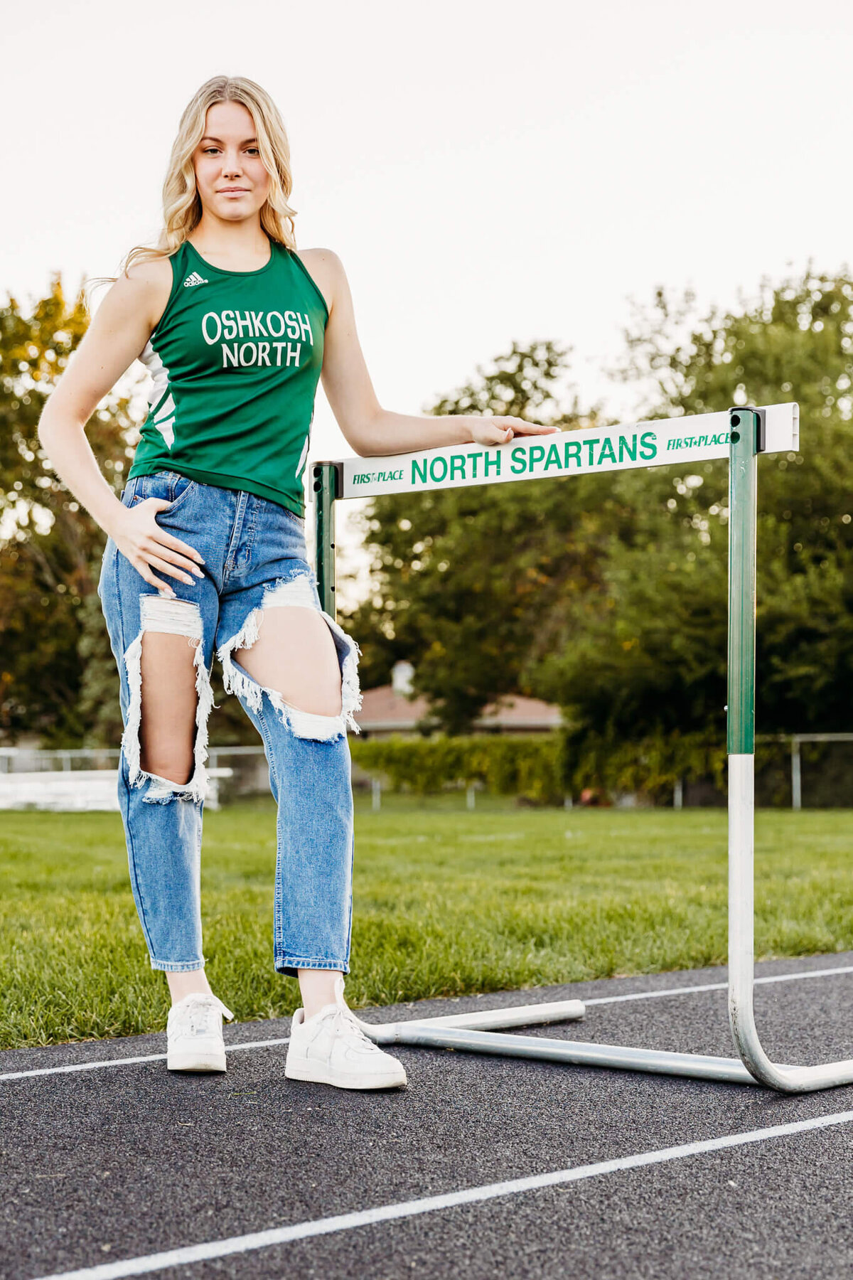 Oshkosh North high school girl leaning against a hurdle while standing on the track at sunset