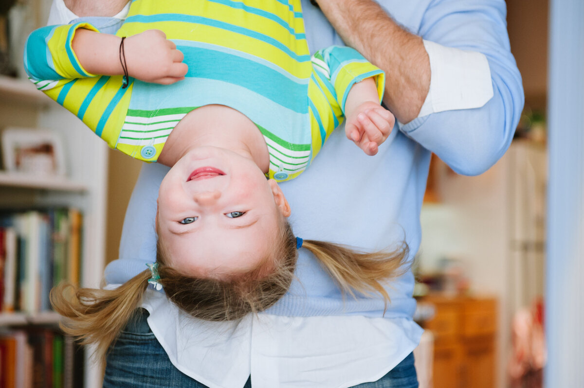 A small girl with pig tails behind held upside down.