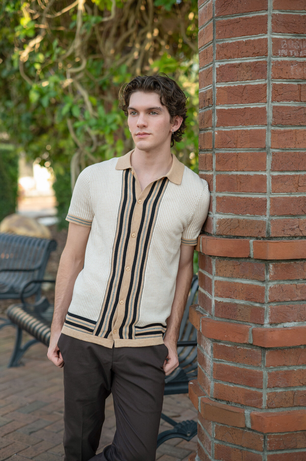 High school senior boy leaning against brick pillar looks away from camera.