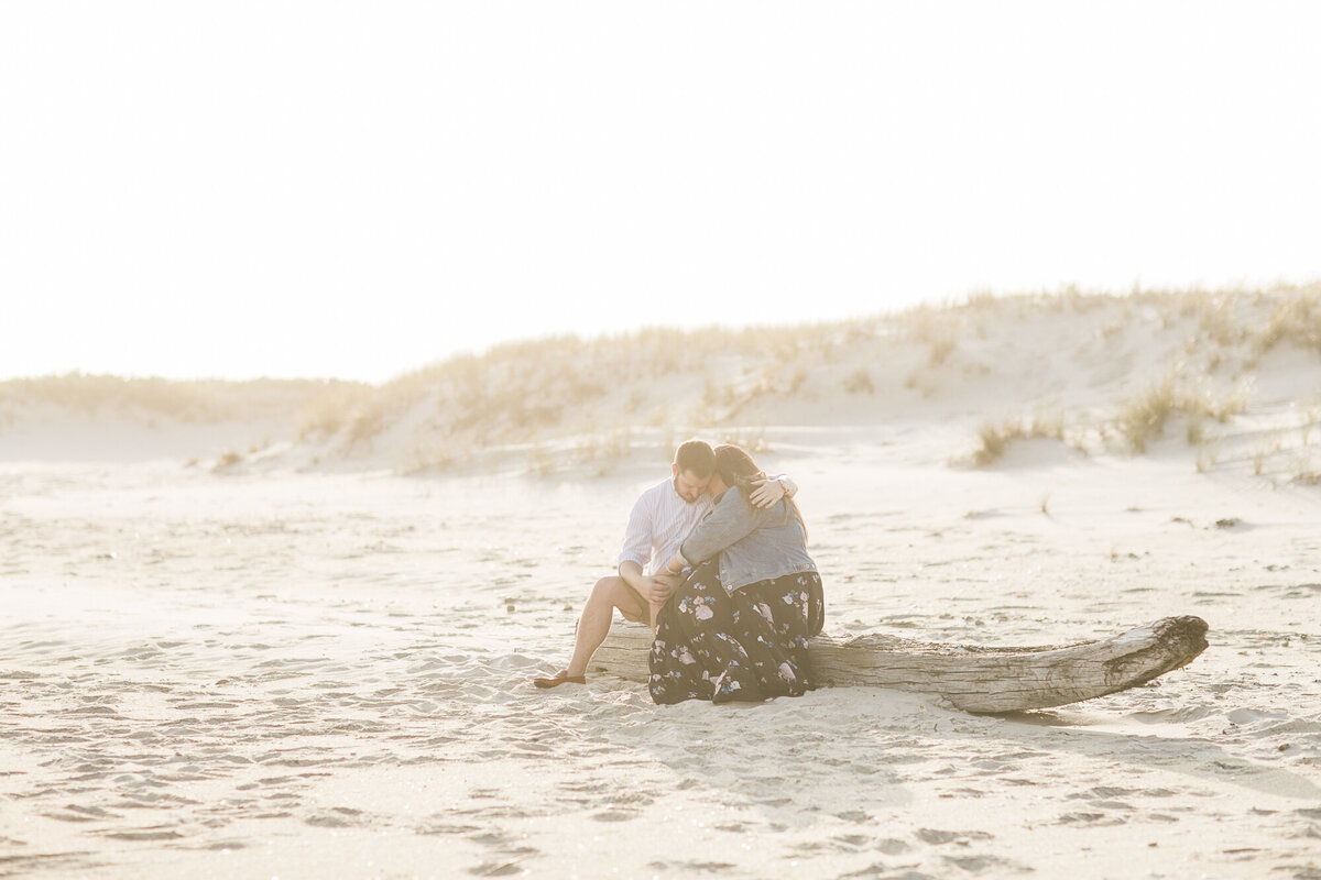 couple sits on a log in the sand at the beach