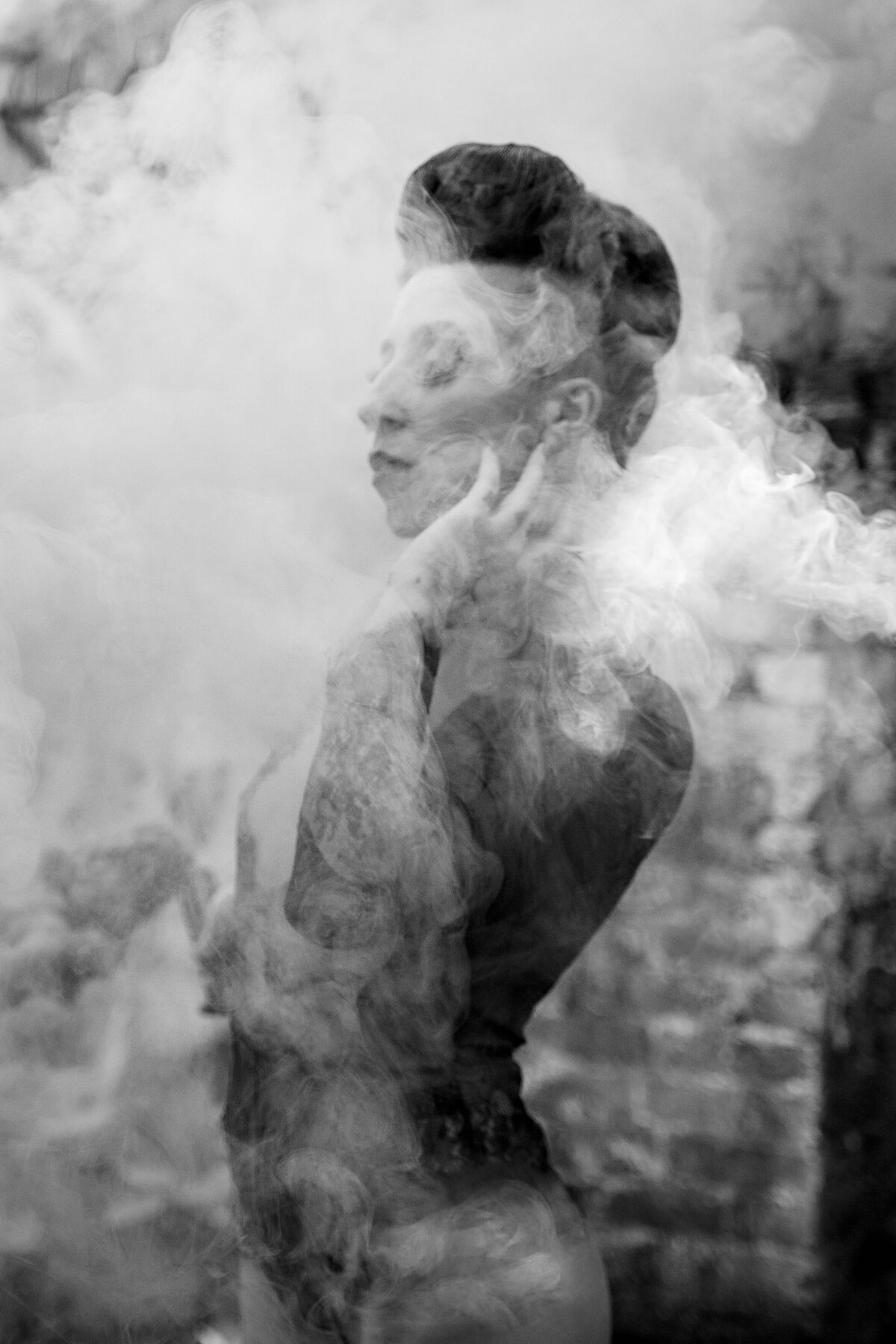 A person with their back arched and their hand up by their face with smoke in front of them.
