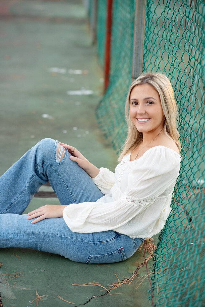 Senior session of young woman sitting against a fence
