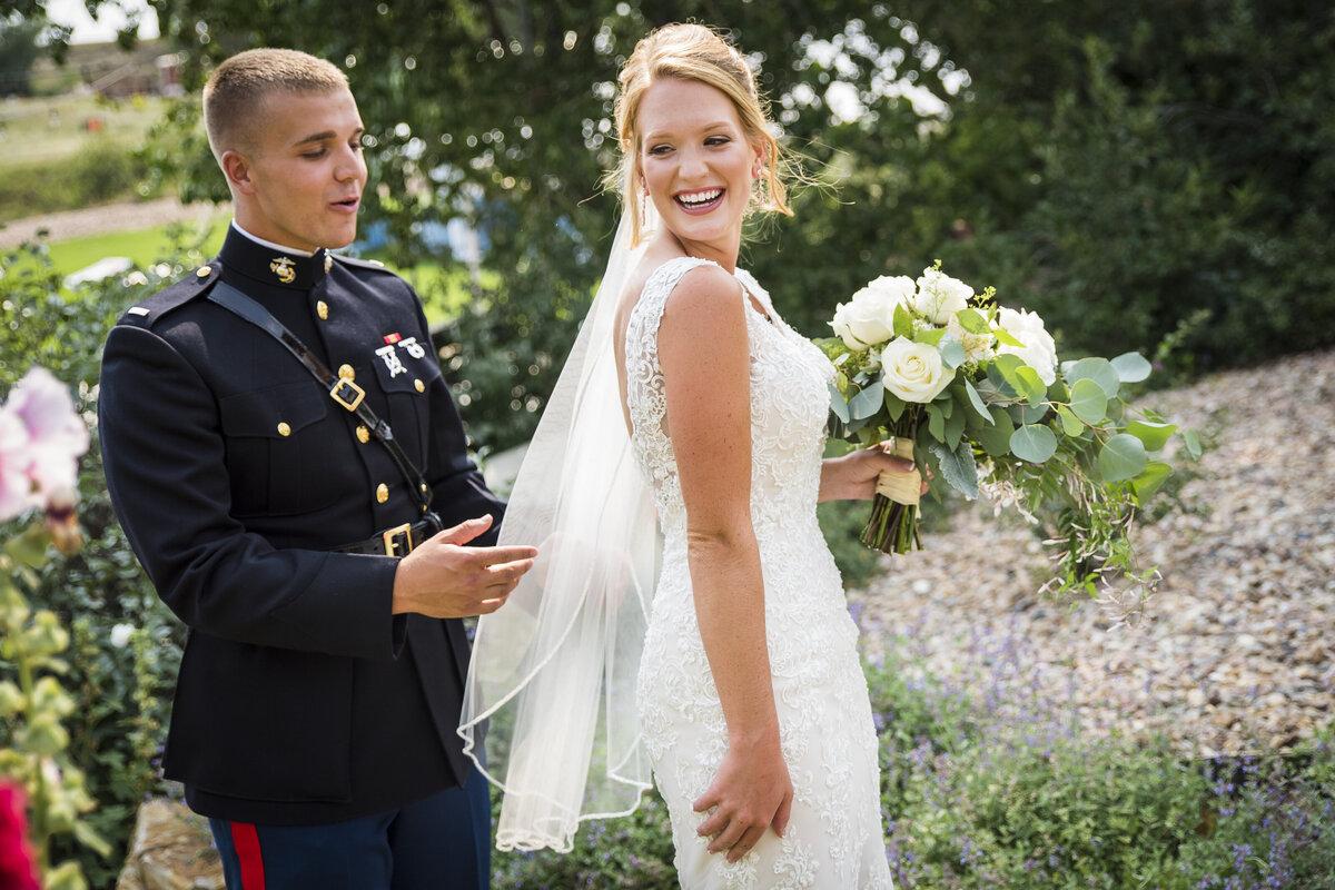 A groom dressed in his military uniform admires his bride's veil as during their first look.