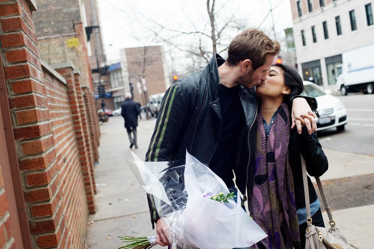 a man and woman kiss in the street while walking during their engagement photos
